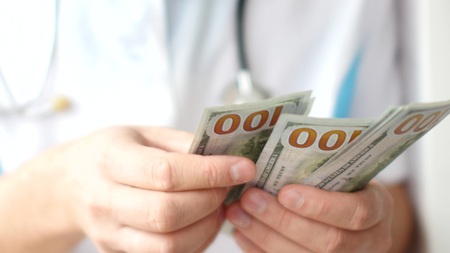 Male doctor counting dollars close-up. Corruption in medicine.の写真素材