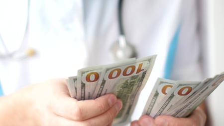 Male doctor counting dollars close-up. Corruption in medicine.の写真素材