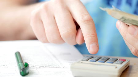 Man counting dollars and filling tax form. He calculating expenses and writing on tax documentの写真素材