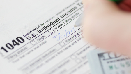 Man counting dollars and filling tax form. He calculating expenses and writing on tax document