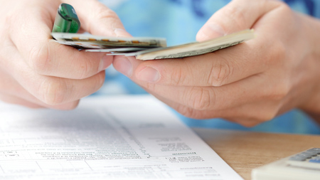 Man counting dollars and filling tax form. He calculating expenses and writing on tax documentの写真素材
