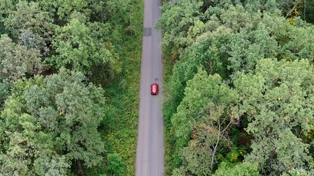 Aerial view of red car driving on country road in forest.の写真素材