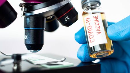 Medical doctor or laborant holding tube with covid vaccine and microscope. Coronavirus 2019-nCoV COVID concept.の写真素材