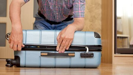 A man trying to pack overfilled suitcaseの写真素材