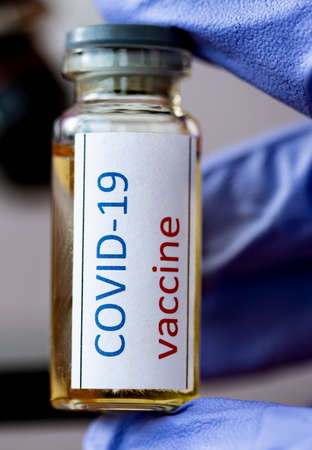 Medical doctor or laborant holding tube with covid-19 vaccine and microscope.