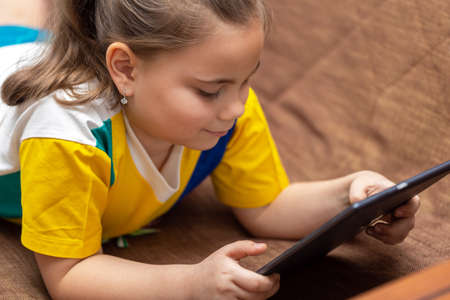 Cute child girl playing with tablet computer on the sofa at the homeの写真素材