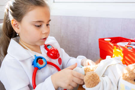 Child girl wearing in white medical uniform playing with teddy bearの写真素材
