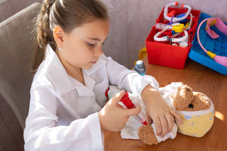 Child girl wearing in white medical uniform playing with teddy bearの写真素材