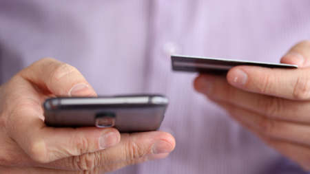 Young man using his phone holding credit card