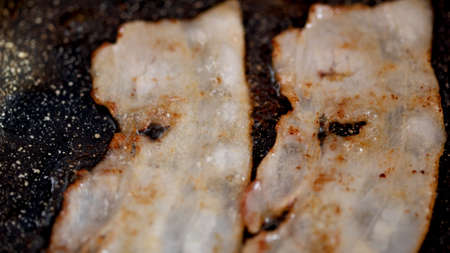 Close up view of bacon slices in frying pan.