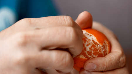 Close-up hands are peeling orange and tasty tangerine.の写真素材