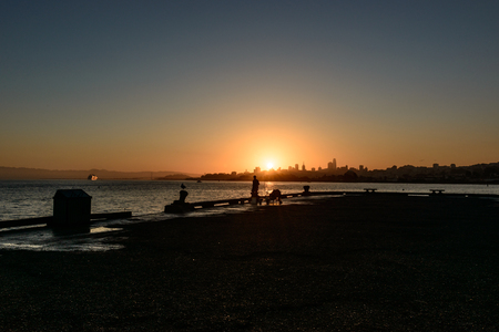 SAN FRANCISCO, USA - OCTOBER 12, 2018: Silhouette of a man fishing at sunrise with downtown background in San Franciscoのeditorial素材