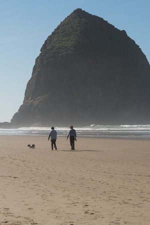 Tourists with a dog  enjoying the beach with Haystack Rock in the background at Cannon beach, Oregon, USA.のeditorial素材