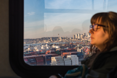Views of Seattle Bay and major buildings at sunset from the window of a public bus on which a young woman rests.のeditorial素材