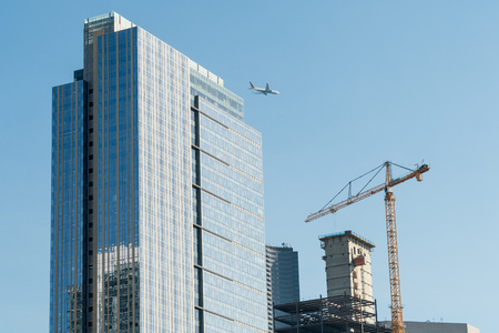 A commercial airplane overflies between a skyscraper and a crane in the Seattle sky.