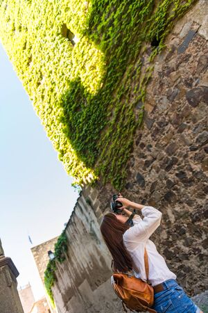 A young red-haired tourist takes a photograph of a tower covered in green ivy in the old town of...
