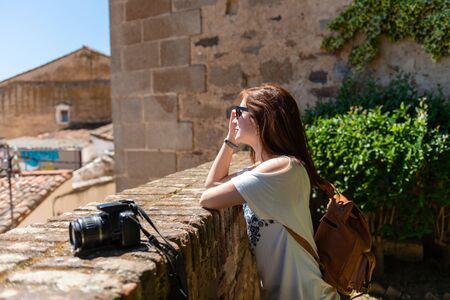 A red-haired young woman with a backpack and camera watches the landscape from a viewpoint in the...