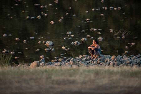 A woman sitting on the rounded stone of the river where Lost Theory psytransce music festival held in Riomalo de Abajoのeditorial素材