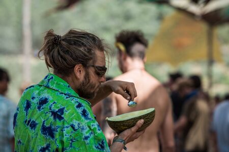 A man refreshes himself by eating a melon with spoons at the Lost Theory psytrance festival in Riomalo de Abajoのeditorial素材