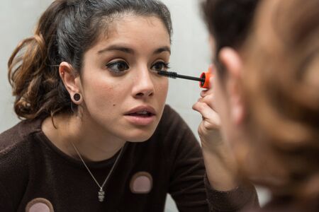 Young woman applies eyelash mascara in front of the mirror in the bathroom.