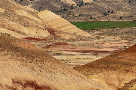 Cars in the distance crossing the deserted, wavy and colorful landscape of Painted Hillsの写真素材