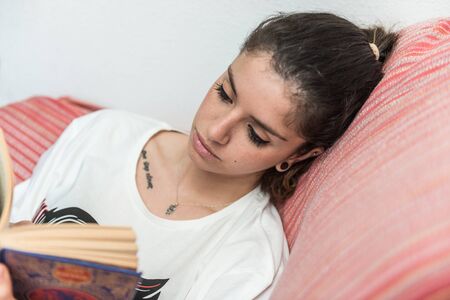 Dark-haired girl quietly reads a book sitting on the couch.の写真素材