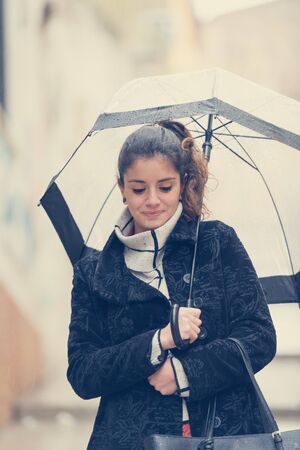 Dark-haired young woman walks through the streets of Caceres with a transparent umbrella on a rainy dayの写真素材