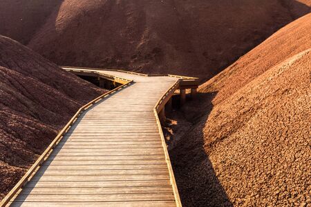 Wooden walkway between the mounds of earth cracked red at Painted Cove Trail Painted Hills