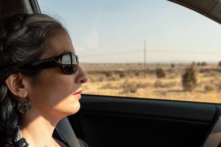 A young brunette woman with gray locks and sunglasses driving a car on Highway 26の写真素材