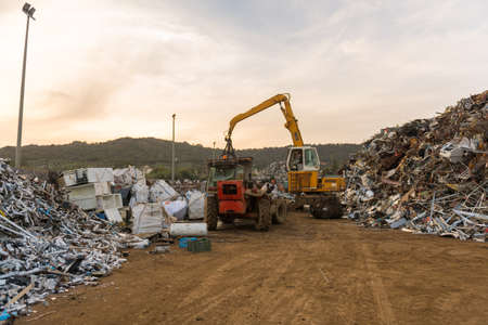 Sunset view of a crane and mountains of scrap metal in a junkyard near Sierra de Fuentes, Extremadura, Spain.のeditorial素材