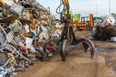 A crane clamp next to a mountain of metal waste in a junkyard.のeditorial素材