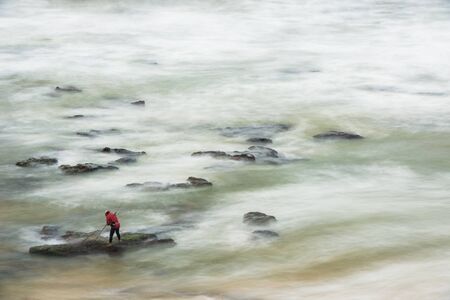 Long exposure photograph of a shellfisherman working on the rocks at Seixo beach, Torres Vedrasの写真素材