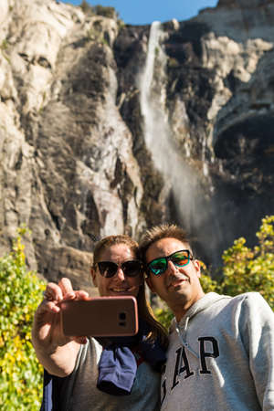 A couple makes a selfie with their smartphone from the base of the Bridalveil waterfall in Yosemite...