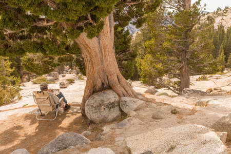 A man sitting in a folding chair takes notes in a notebook at Olmsted Point in Yosemite National Parkのeditorial素材
