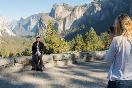 A couple takes pictures at the Tunnel View point in Yosemite National Park in the background, California, USAのeditorial素材