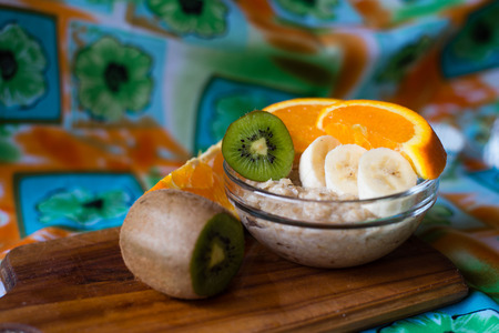 oatmeal, orange, banana, kiwi on wooden boardの写真素材