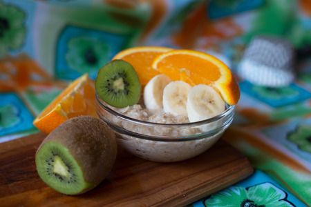 oatmeal, orange, banana, kiwi on wooden boardの写真素材