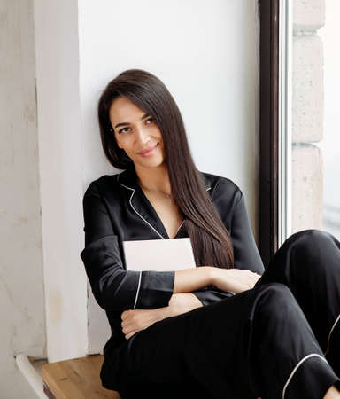Portrait of a happy mid adult woman sitting by window at home. Relaxed woman smilingの写真素材