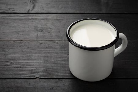 Black weathered wooden board with white tin cup with milk as image background with copy-space.の写真素材