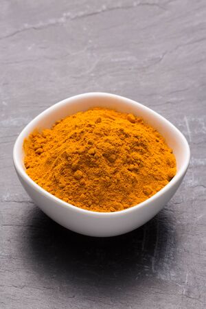 Kurkuma spice powder in white bowl on dark slate background, closeup.の写真素材