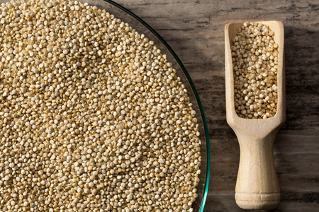 Quinoa in glass dish on wooden background with spice shovel, detail view from above.の写真素材