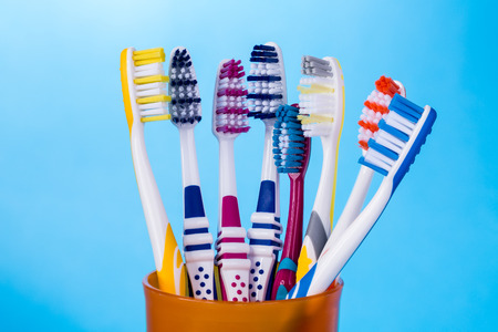 Various colorful toothbrushes in orange cup on blue background.の写真素材