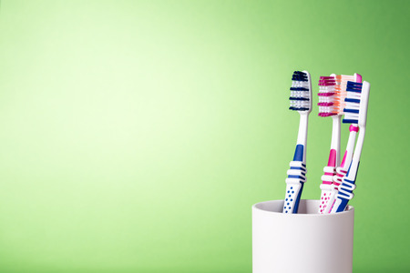 Various toothbrushes in white cup on light green background with copy space on the left side.の写真素材