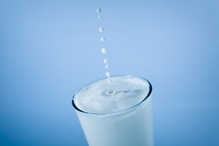 Milk glass with falling drops and splash on blue background, closeupの写真素材