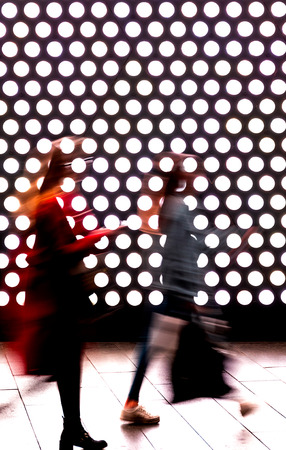 Two blurred pedestrians women in urban scene with bright backlight in a shopping mall at night