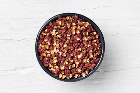 Szechuan pepper in cast-iron round mug on white wooden background, view directly from above.