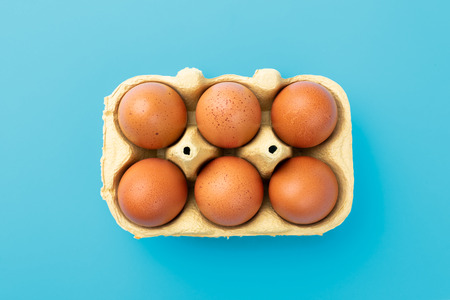 Six brwon eggs in mould box on blue turquoise background, view from above