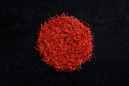 Circular heap of saffron crocus threads on black slate background, view from above