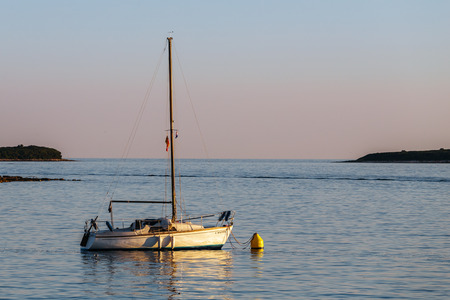 Lonely boat with a flat sail standing in the sea at sunset and the islands.