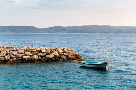 The same fishing boat in calm sea water at sunset near the stone pier in Croatia, Brelaの写真素材